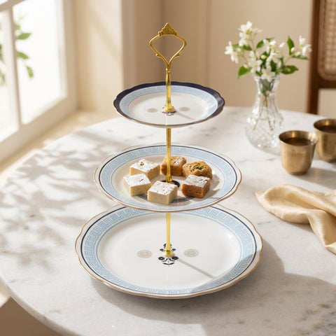 Three-tiered decorative plate with pastries on a marble table with a vase of flowers in the background.