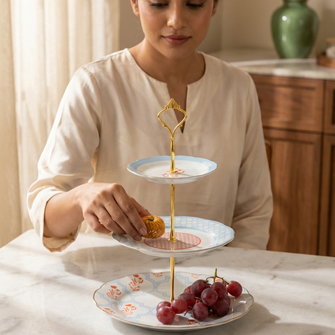 Woman arranging food on a three-tiered cake stand in a kitchen setting.
