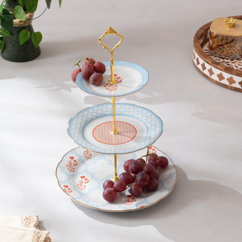 Three-tiered ceramic stand with decorative plates holding grapes on a light surface.