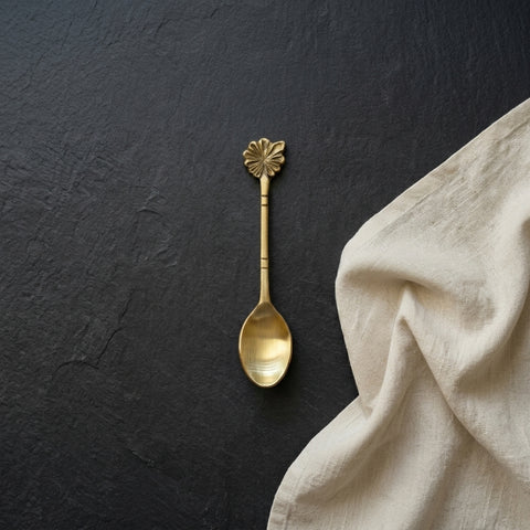 Gold spoon with decorative handle on a dark surface next to beige fabric