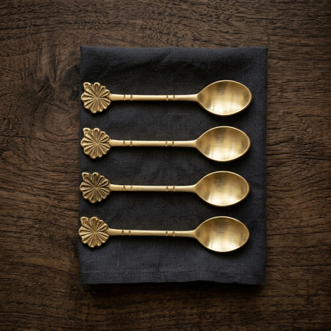 Set of four gold spoons with decorative handles on a dark napkin against a wooden background