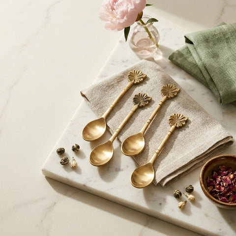 Set of gold spoons on a marble surface with a pink flower and green napkin.