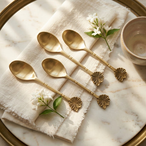 Set of gold spoons on a marble surface with a white napkin and flowers.