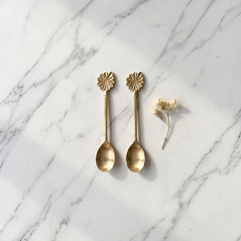 Two gold spoons with decorative ends on a marble surface.