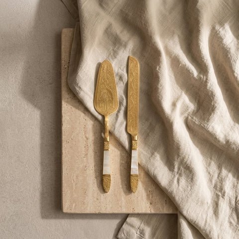 Two gold-handled knives on a stone surface with a beige cloth.