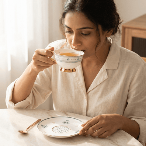 A woman sipping her tea from bone china tea cup and saucer 