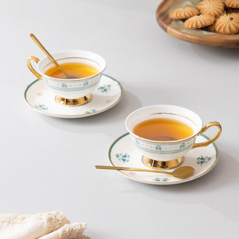 Two elegant teacups with gold handles on saucers, filled with tea, on a light surface.