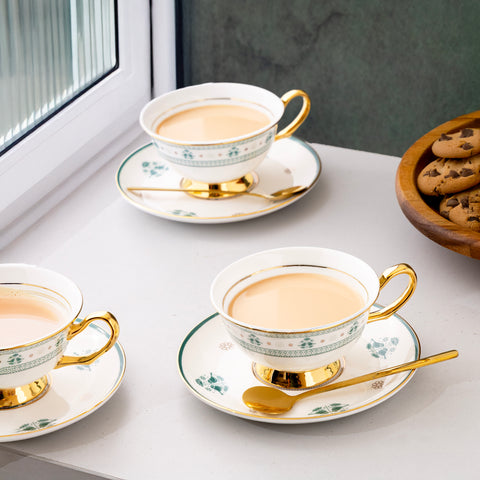 Tea cups with gold handles on saucers on a table with cookies in the background.