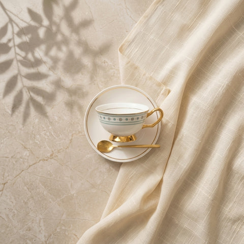 Teacup with saucer and spoon on a marble surface with fabric and leaf shadows