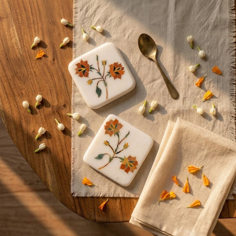Two square cookies with floral designs on a wooden surface with a napkin and spoon.
