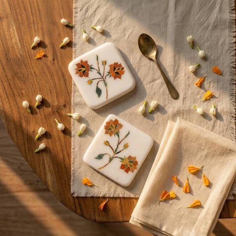 Two square cookies with floral designs on a wooden surface with a napkin and spoon.
