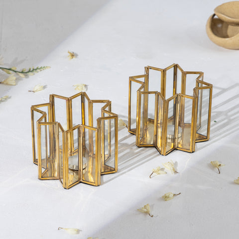 Gold geometric candle holders on a white surface with scattered flowers.