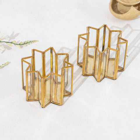 Gold geometric candle holders on a white surface with a subtle floral pattern.