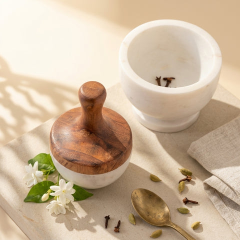 Wooden and marble pestle and mortar with spices and flowers on a light surface