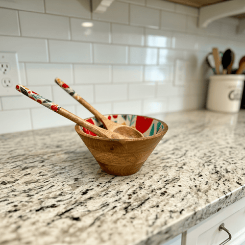 Two mango wood salad servers with floral handles resting across the wooden bowl