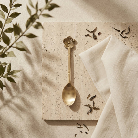 Gold spoon on a textured surface with a white cloth and plant leaves in the background