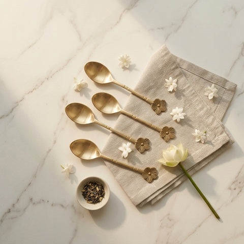 Set of gold spoons on a marble surface with flowers and a napkin.