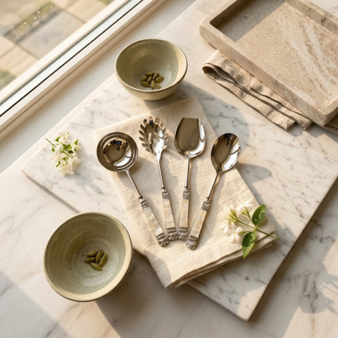 Set of stainless steel serving Spoon Set with mother of pearl inlays on a marble surface with bowls and flowers.