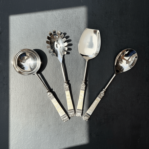 Set of decorative mother of pearl serving Spoon Set on a dark surface with a light gray rectangular block.