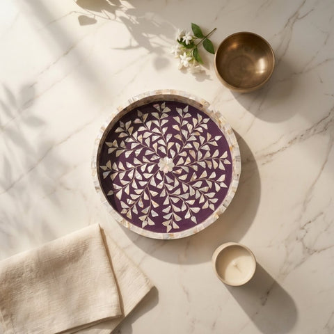 Decorative purple plate with white patterns on a marble surface with a gold bowl and white flowers.