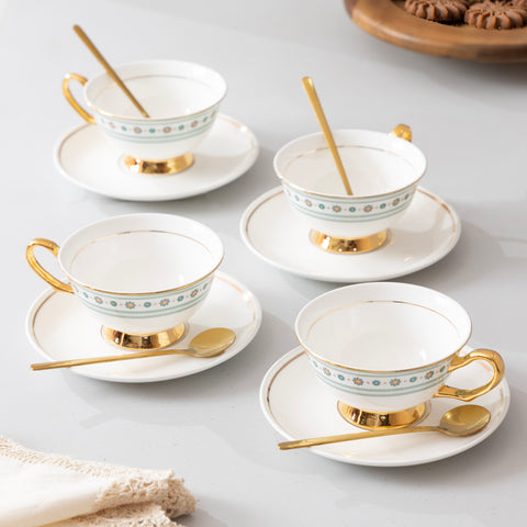 Set of four white tea cups with gold trim and saucers on a light gray surface.