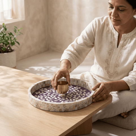 Woman in a white outfit sitting on the floor, holding a small cup over a violet round tray with mother of pearl inlay