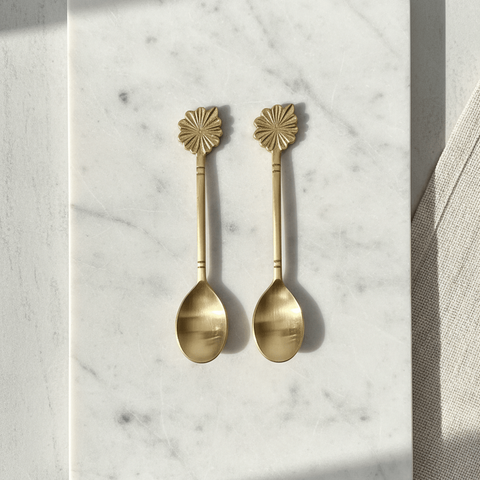Two brass spoons with decorative ends on a marble surface