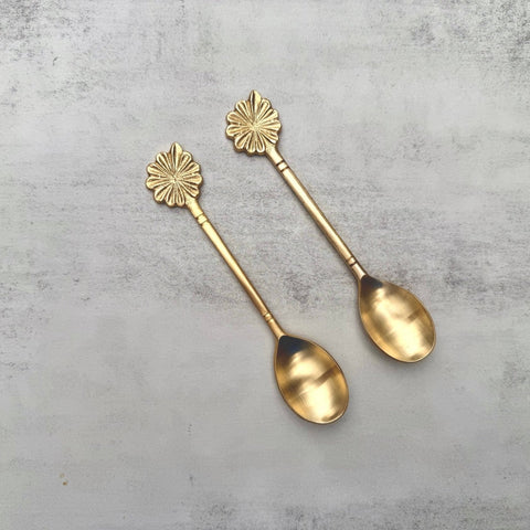 Two brass dessert spoons with decorative handles on a gray surface