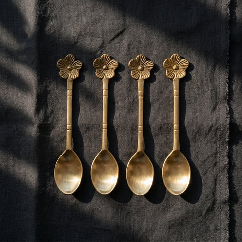 Four gold spoons with floral ends on a dark fabric background