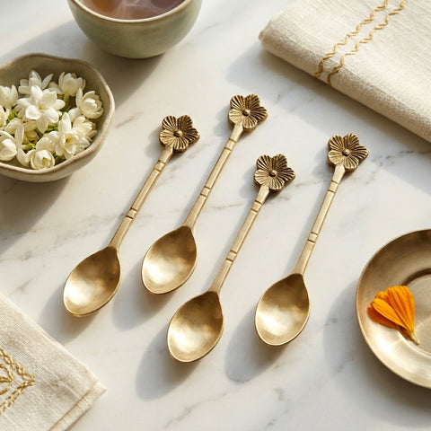 Set of gold floral spoons on a marble surface with a bowl of flowers and a cup.
