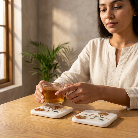 Woman placing a cup of tea on a marble coaster set featuring floral stone inlays.