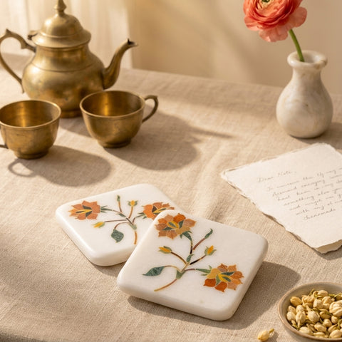 Decorative marble coaster set with floral stone inlays on a table with tea set and flowers.
