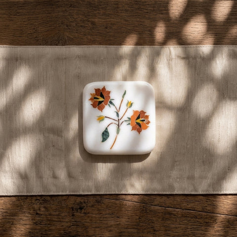 A decorative marble coaster set with floral stone inlays on a napkin kept on a  wooden surface