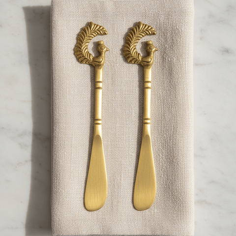 Two butter spreader knives with decorative handles on a beige napkin against a marble background