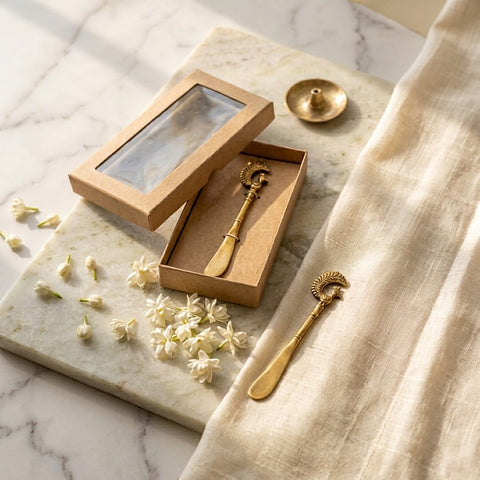 Butter spreader knives in a cardboard box on a marble surface with flowers and a cloth.