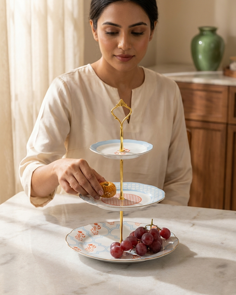 Woman arranging food on a three-tiered serving tray in a kitchen setting.