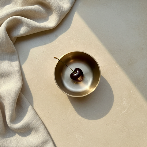 Gold bowl with a cherry on a beige surface with fabric