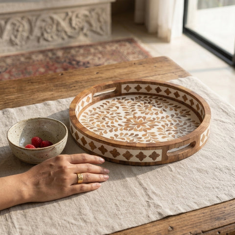 Decorative round wooden serving tray with floral inlay on a table with a bowl of berries.