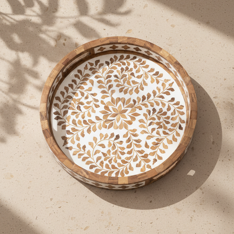 Decorative round wooden serving tray with floral inlay on a beige surface