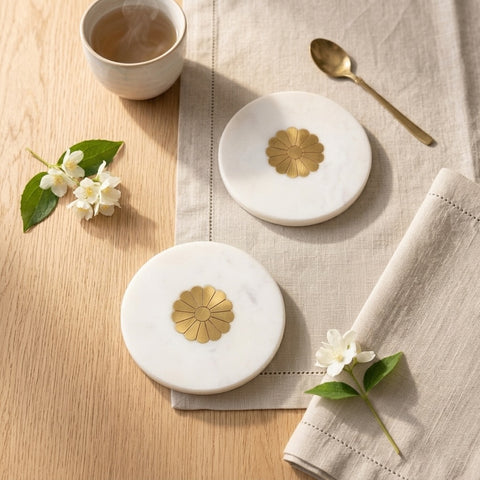 Set of white marble coasters with brass inlays kept on a napkin that is laid on a wooden surface