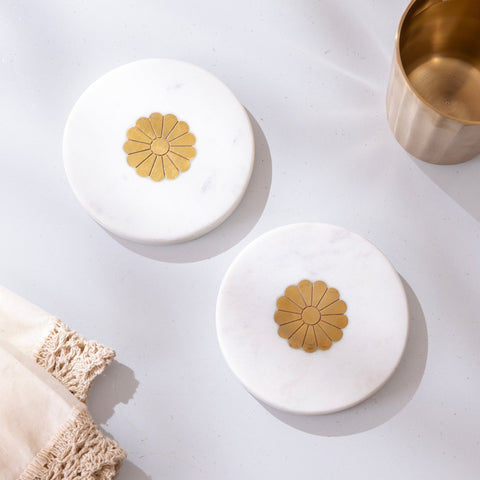 Set of white marble coasters with brass inlays on a light surface.