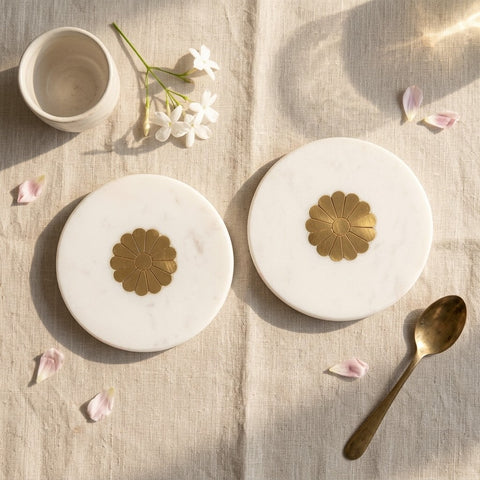 Set of white marble coasters with brass inlays  on a light wooden surface with a spoon and flowers.