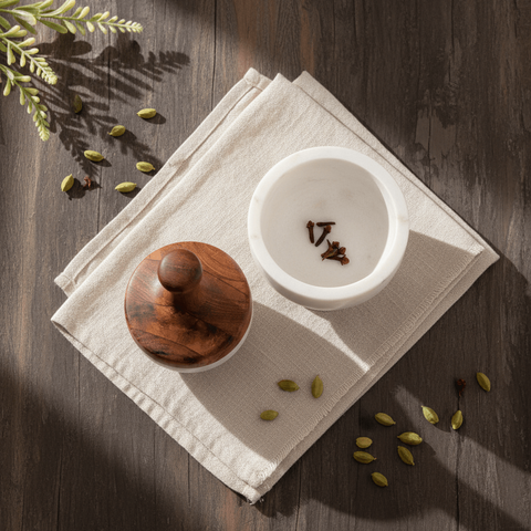 White marble mortar and pestle set on a white napkin on a wooden surface with scattered spices.