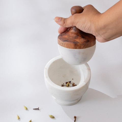 Person grinding spices in a white marble mortar and pestle set with a wooden handle.